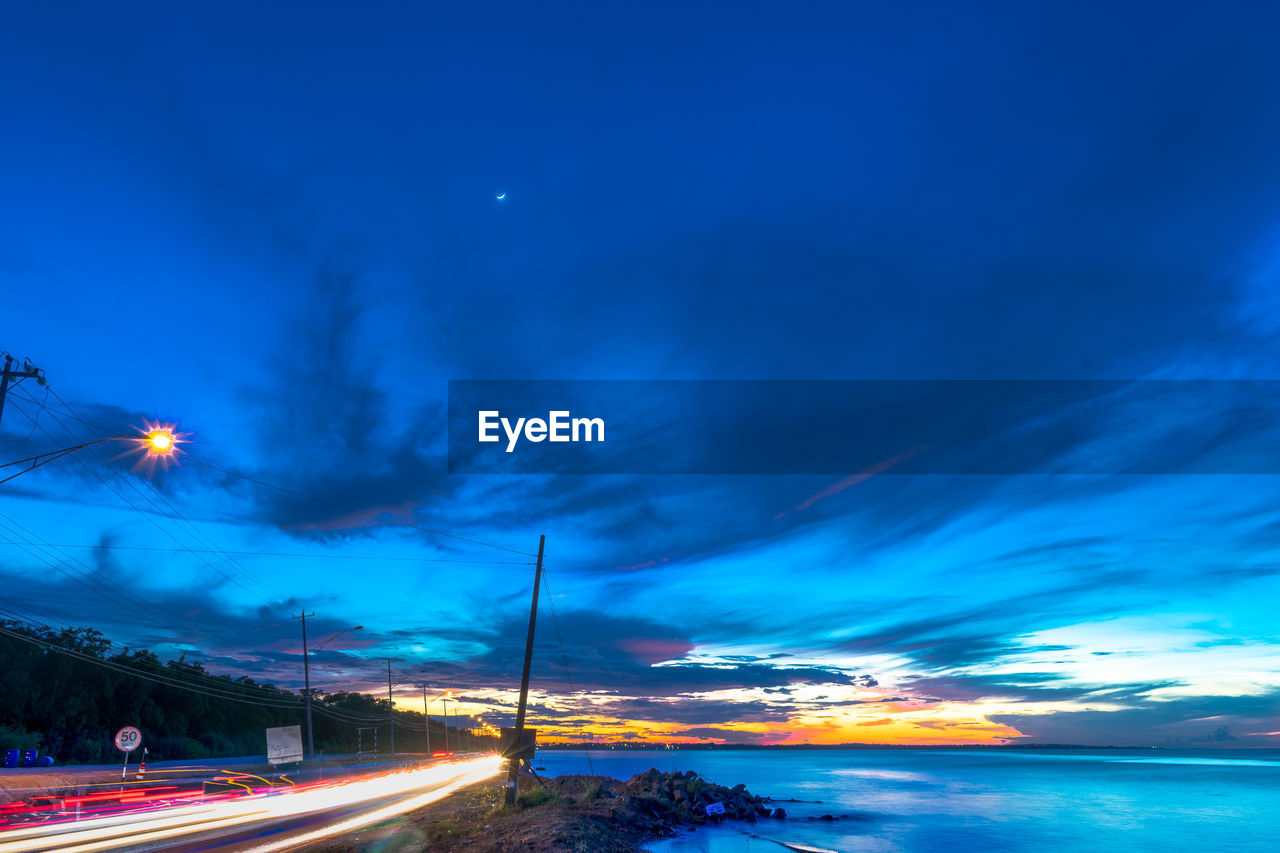 ILLUMINATED LIGHT TRAILS ON ROAD AGAINST SKY AT NIGHT