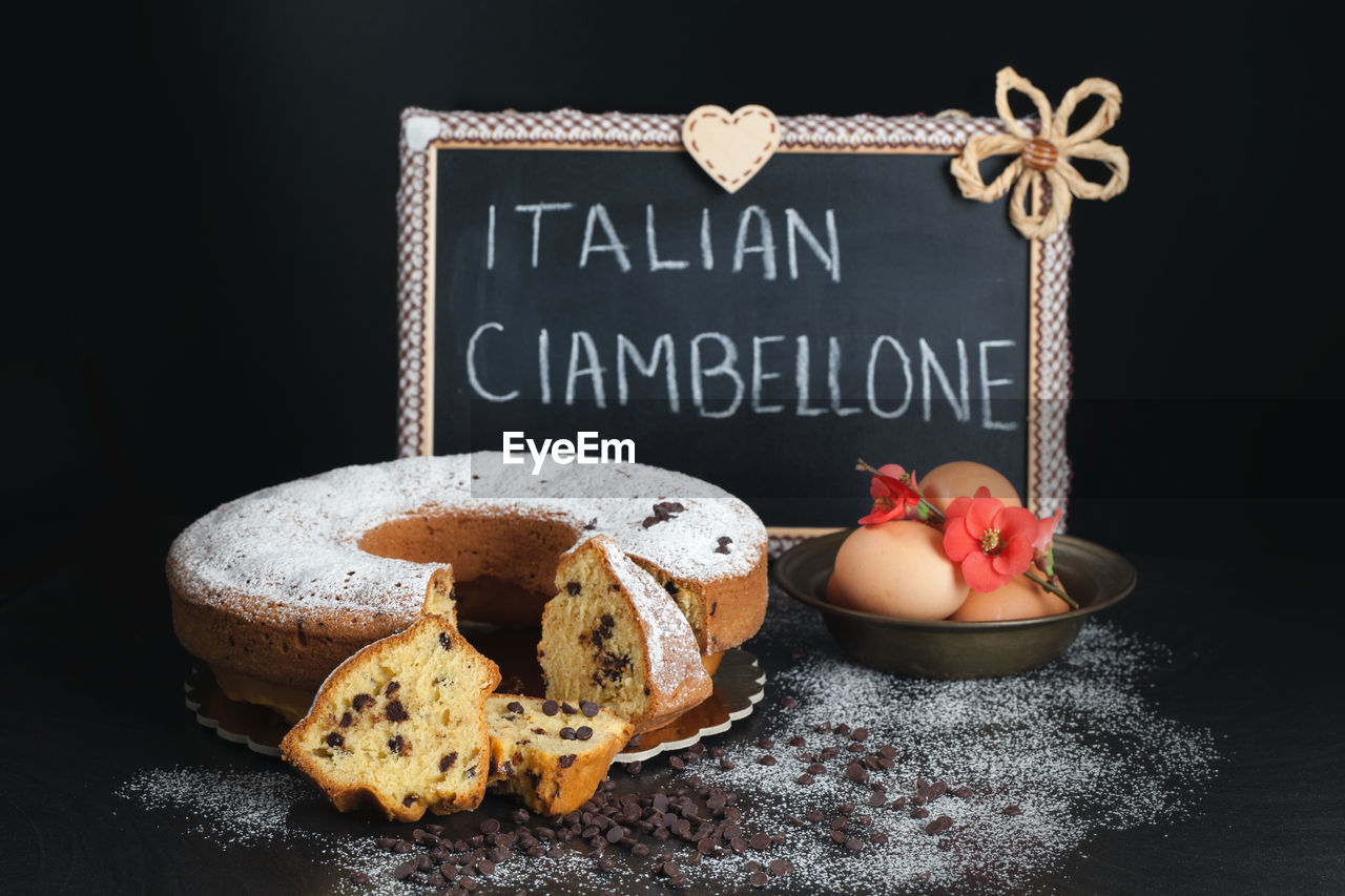 Italian ring cake called ciambellone on black background decorated with eggs flowers and icing sugar