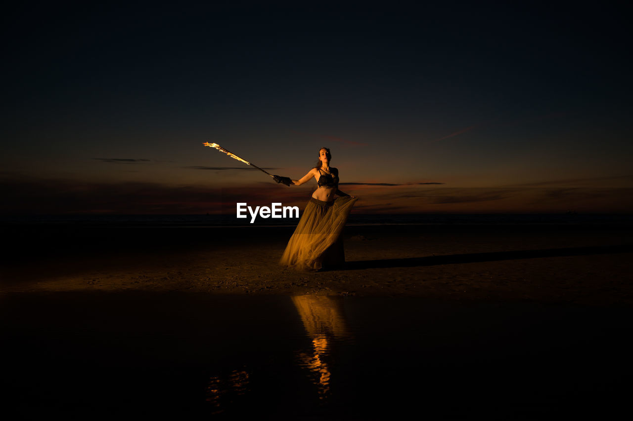 Silhouette woman standing on beach against sky during sunset