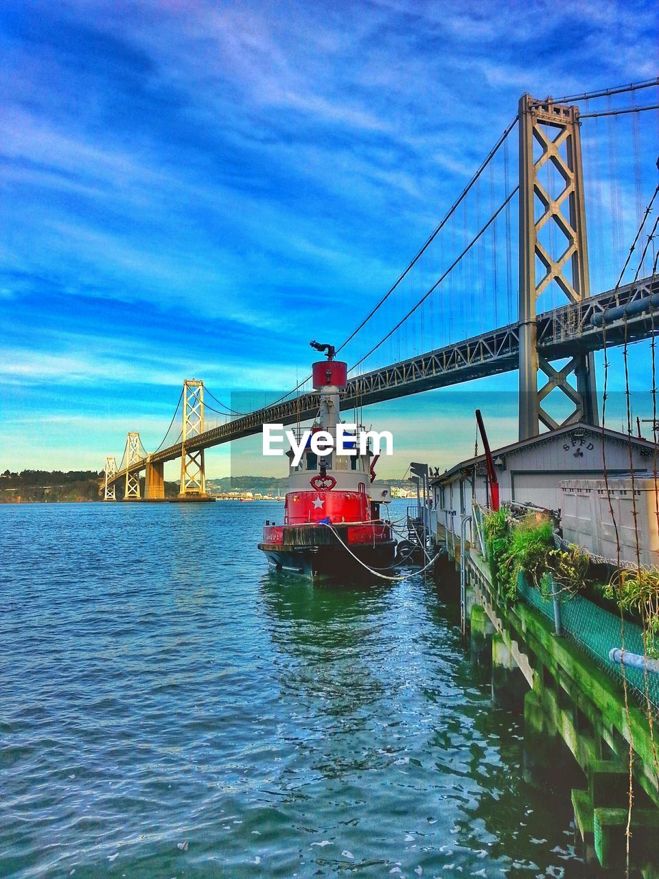 Boat moored on harbor by bay bridge against sky