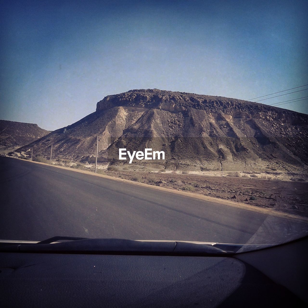 ROAD BY MOUNTAINS SEEN THROUGH CAR WINDSHIELD