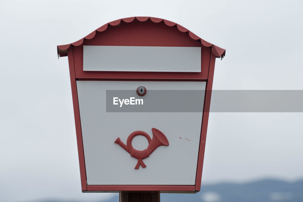 A white european mailbox with post horn and a red frame