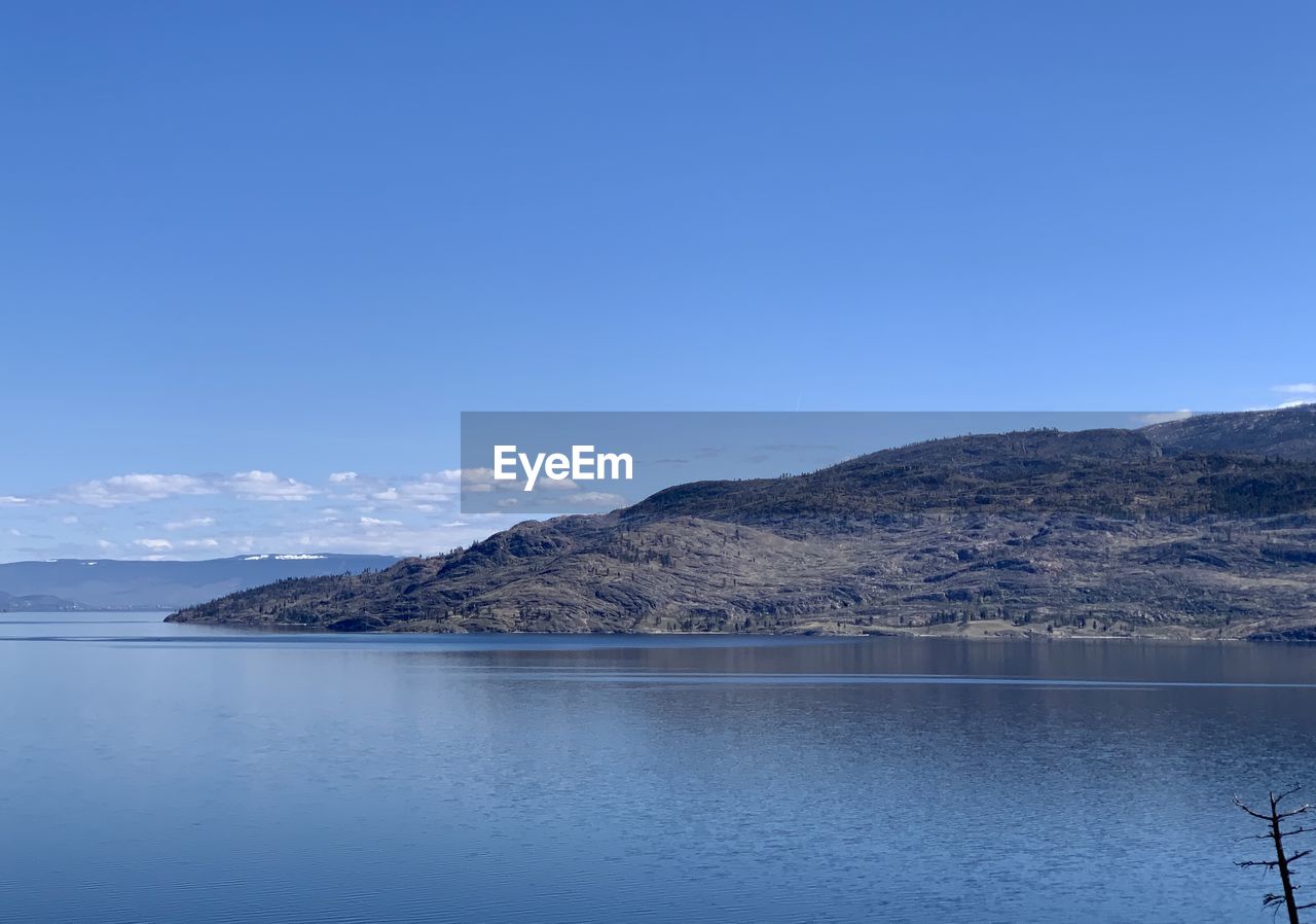 Scenic view of sea and mountains against clear blue sky