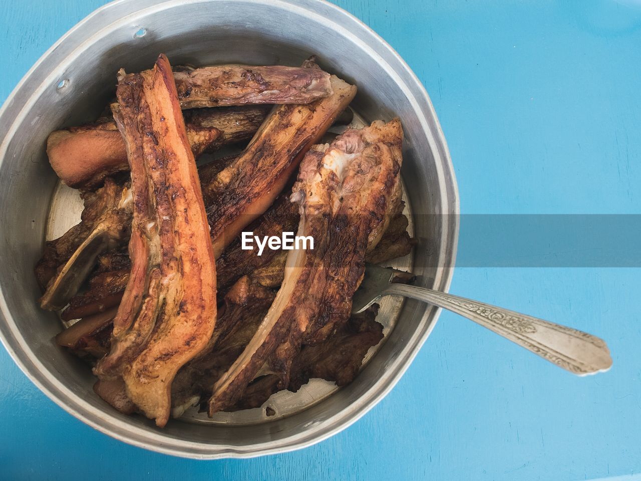 High angle view of pork with spoon in container against blue table