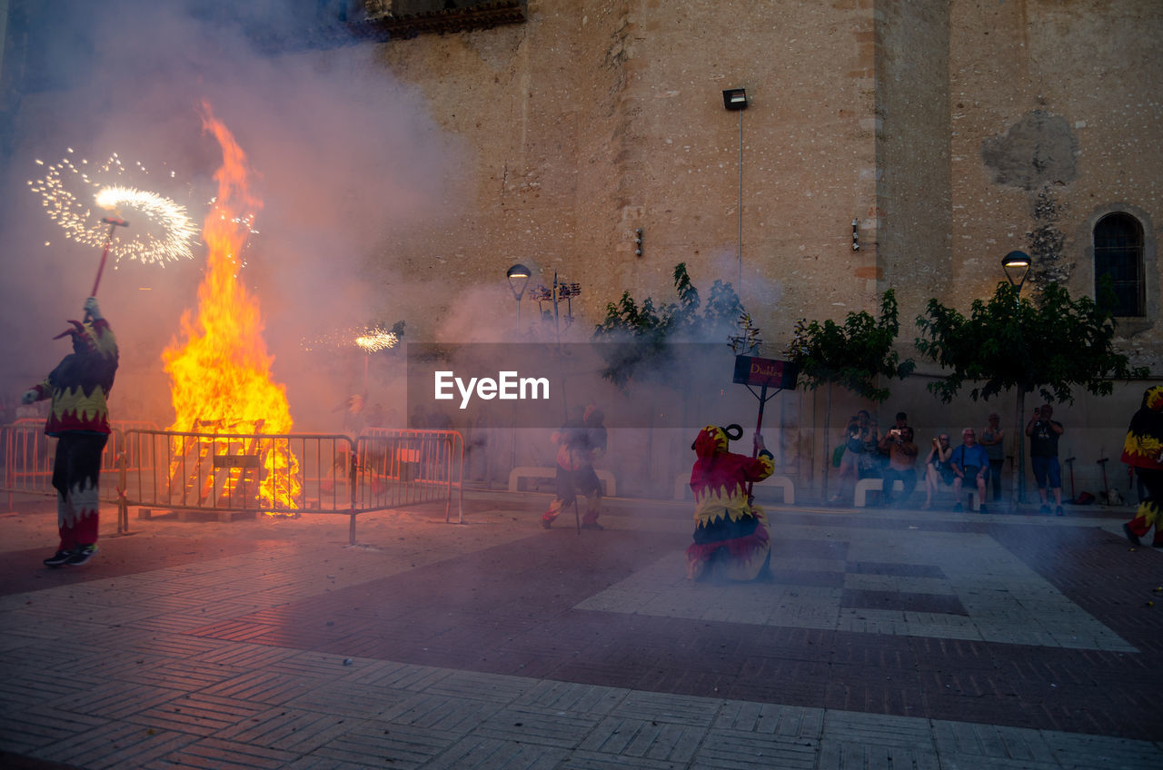 group of people, architecture, city, burning, smoke, celebration, street, fire, building exterior, tradition, men, night, adult, heat, fireworks, nature, built structure, motion, crowd, religion, large group of people, flame, arts culture and entertainment, outdoors, event, women, belief
