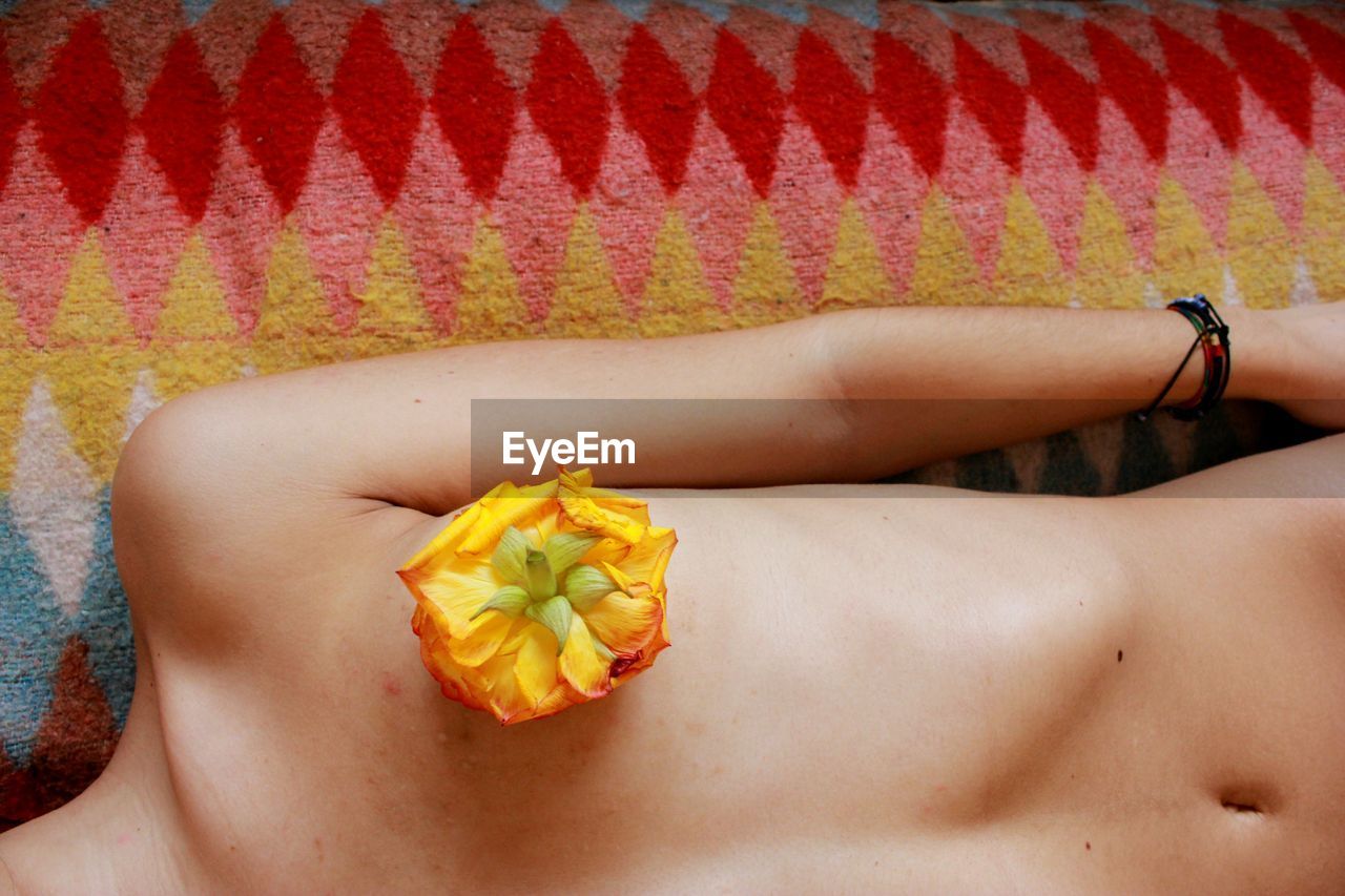 Midsection of woman with flower on breast lying on rug