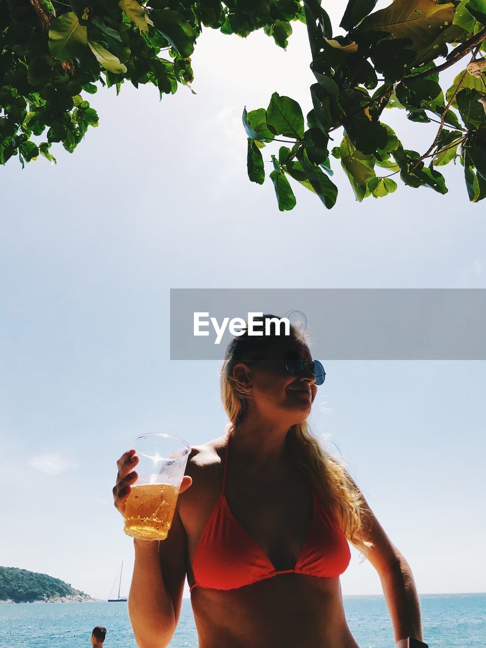 Woman in bikini drinking beer at beach against sky