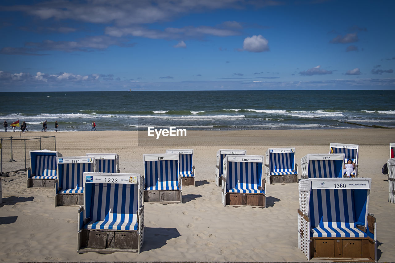 DECK CHAIRS ON BEACH AGAINST SKY