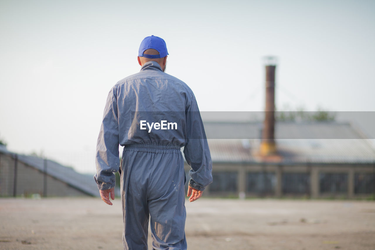 Rear view of worker walking toward factory against clear sky