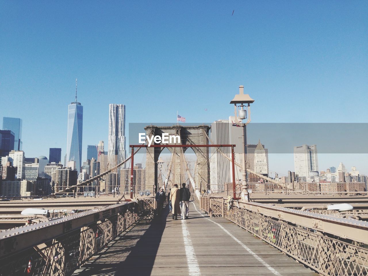 Rear view of people walking on brooklyn bridge by city against clear blue sky