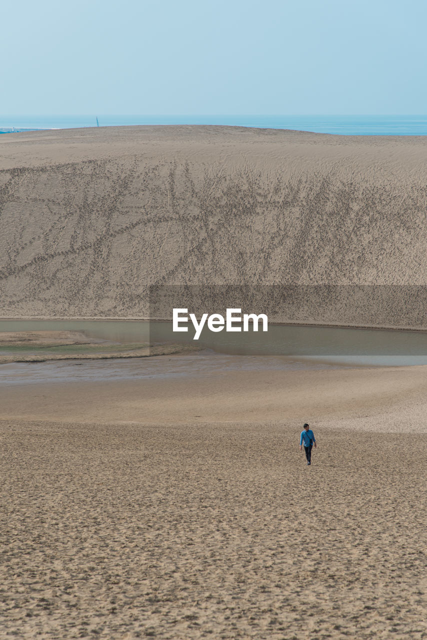 Full length of man walking on sand against clear sky