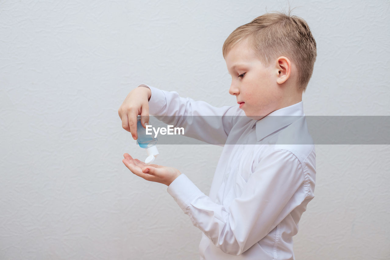 Boy using sanitizer against white wall