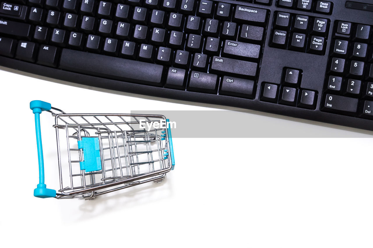 Close-up of laptop keyboard and shopping cart over white background