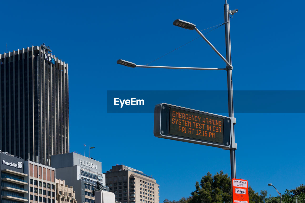Low angle view of road sign by buildings against clear blue sky