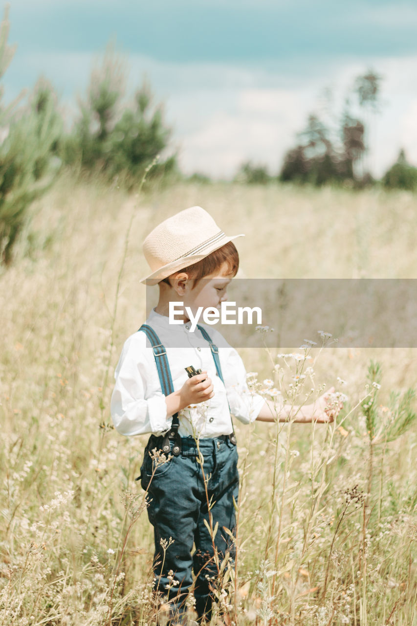 Little farmer on a summer field, cute little boy in a straw hat. boy with a flower 