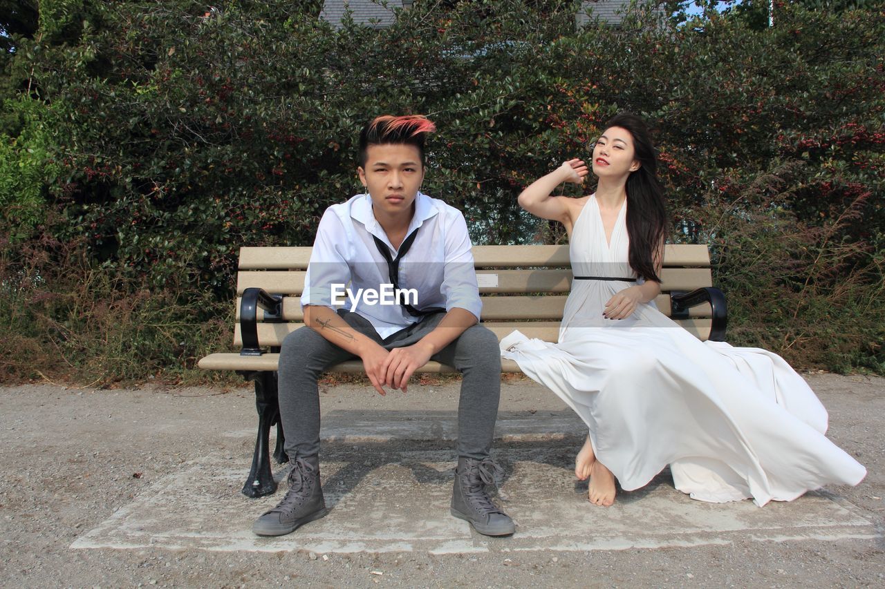 Portrait of young couple sitting on bench in park