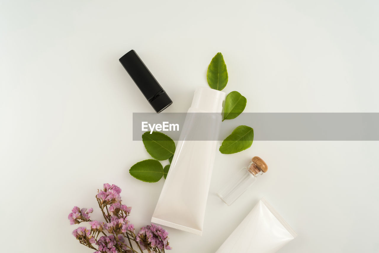 High angle view cream tube with flowers and leaves on table