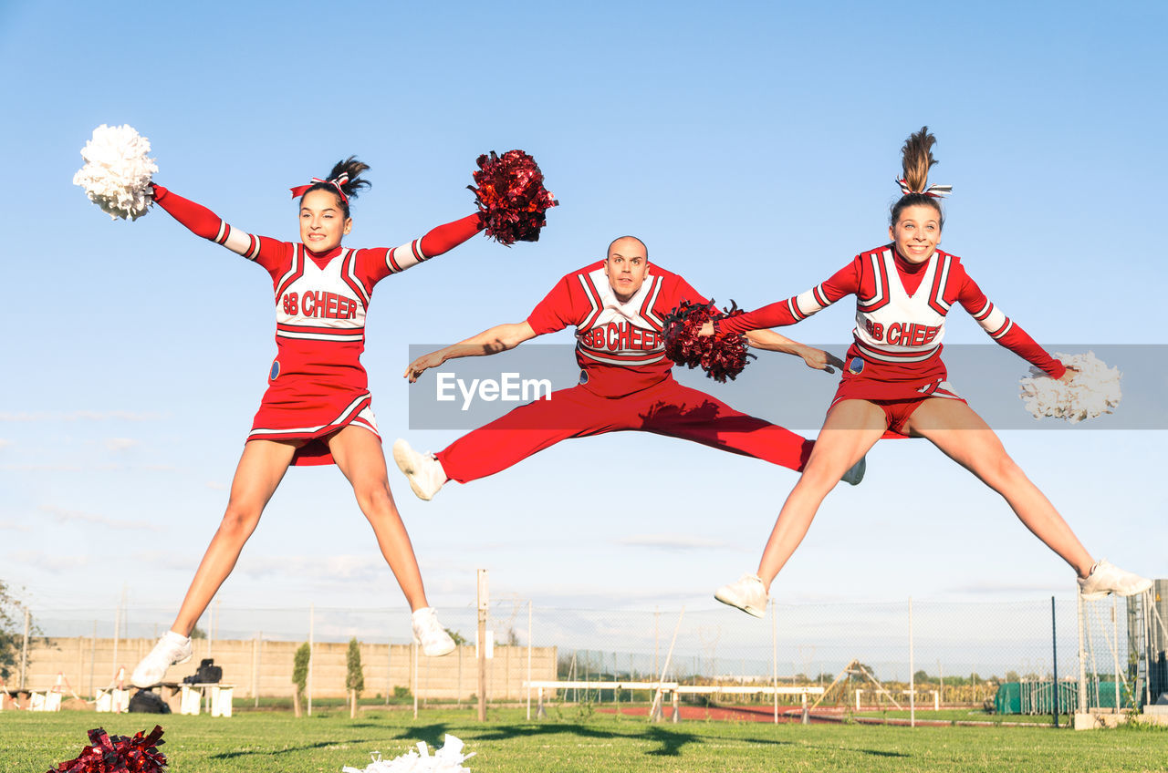 Cheerleaders performing with sportsman on field against blue sky