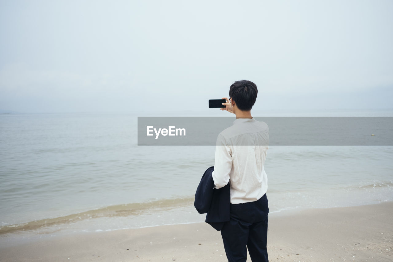 FULL LENGTH REAR VIEW OF MAN STANDING ON BEACH