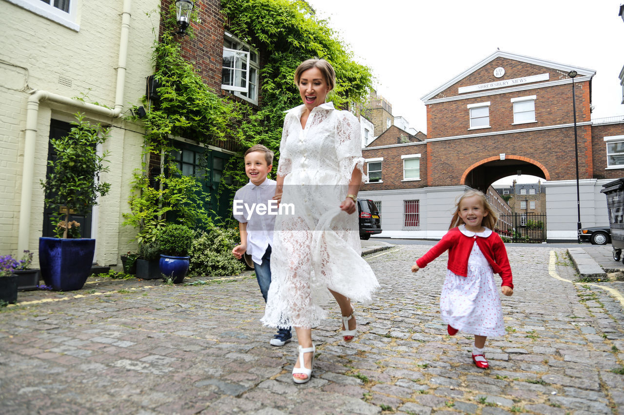 FULL LENGTH OF MOTHER STANDING AGAINST BUILDING