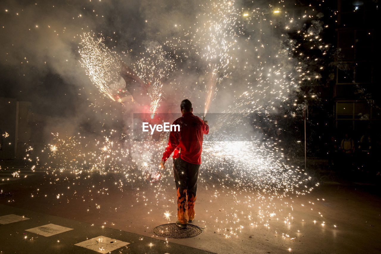 Man with firework display standing on road at night