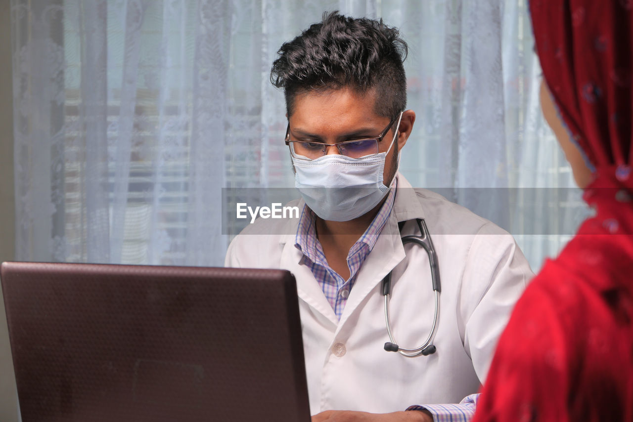 Close-up of doctor wearing flu mask sitting at clinic