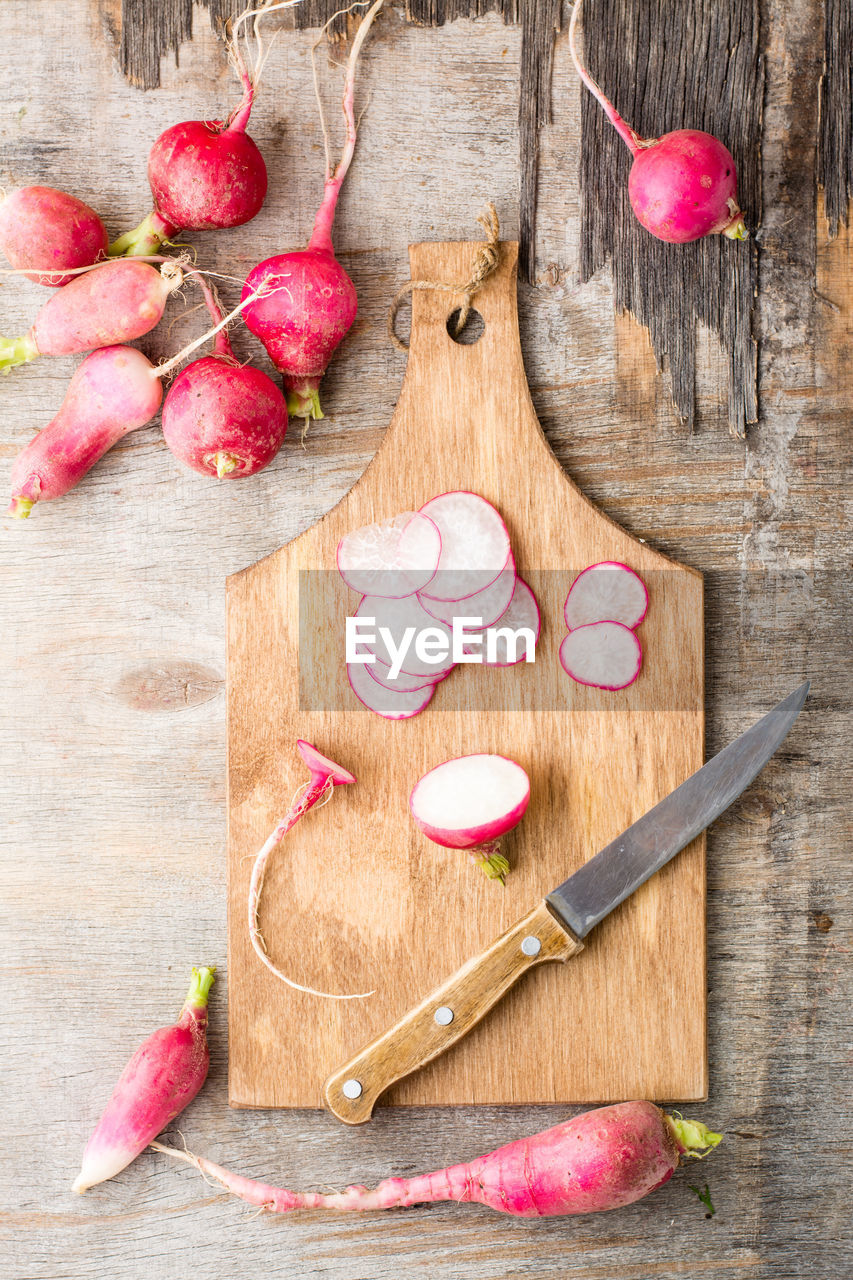 Fresh chopped radishes and a knife on a cutting board on a wooden table