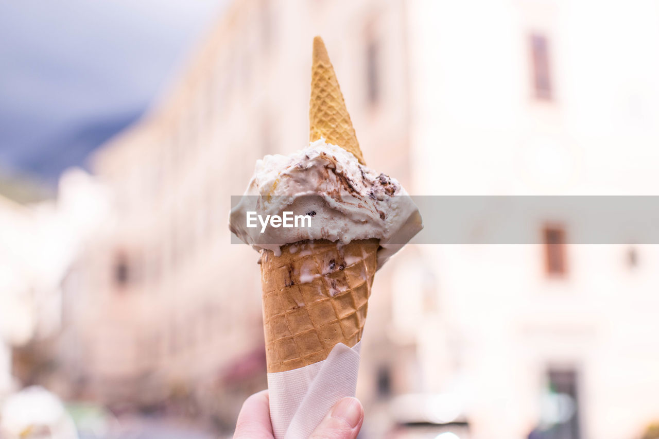 CLOSE-UP OF HAND HOLDING ICE CREAM CONE OUTDOORS