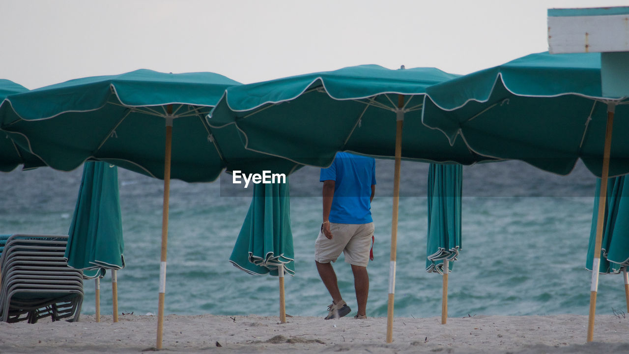 Rear view of man walking by parasols at beach
