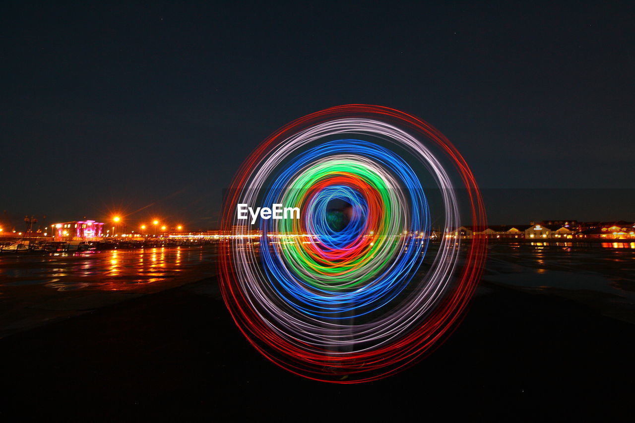 MULTI COLORED LIGHT TRAILS IN CITY AGAINST SKY AT NIGHT