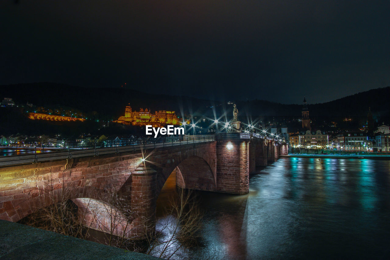 Illuminated old bridge over river neckar and castle against sky at night in heidelberg