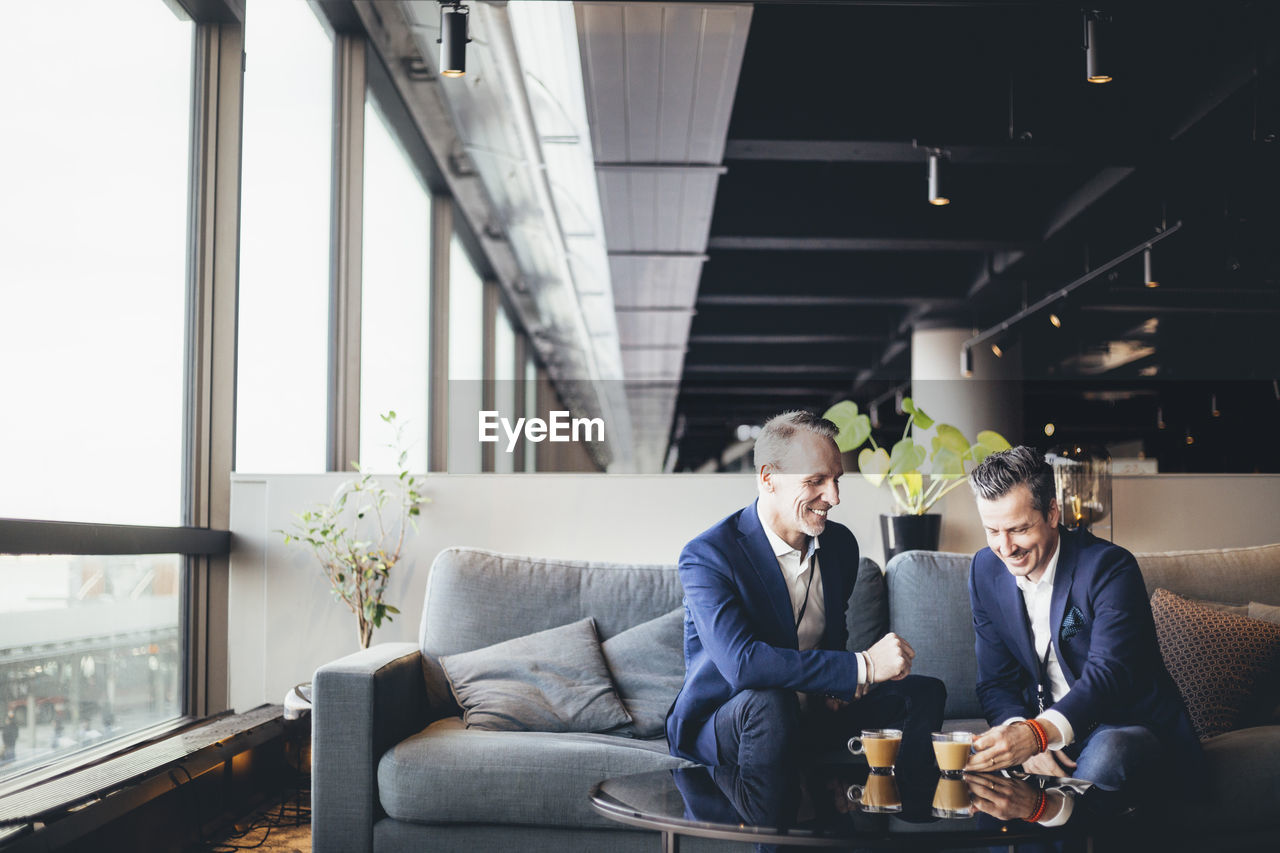 Happy entrepreneurs discussing with tea while sitting in office