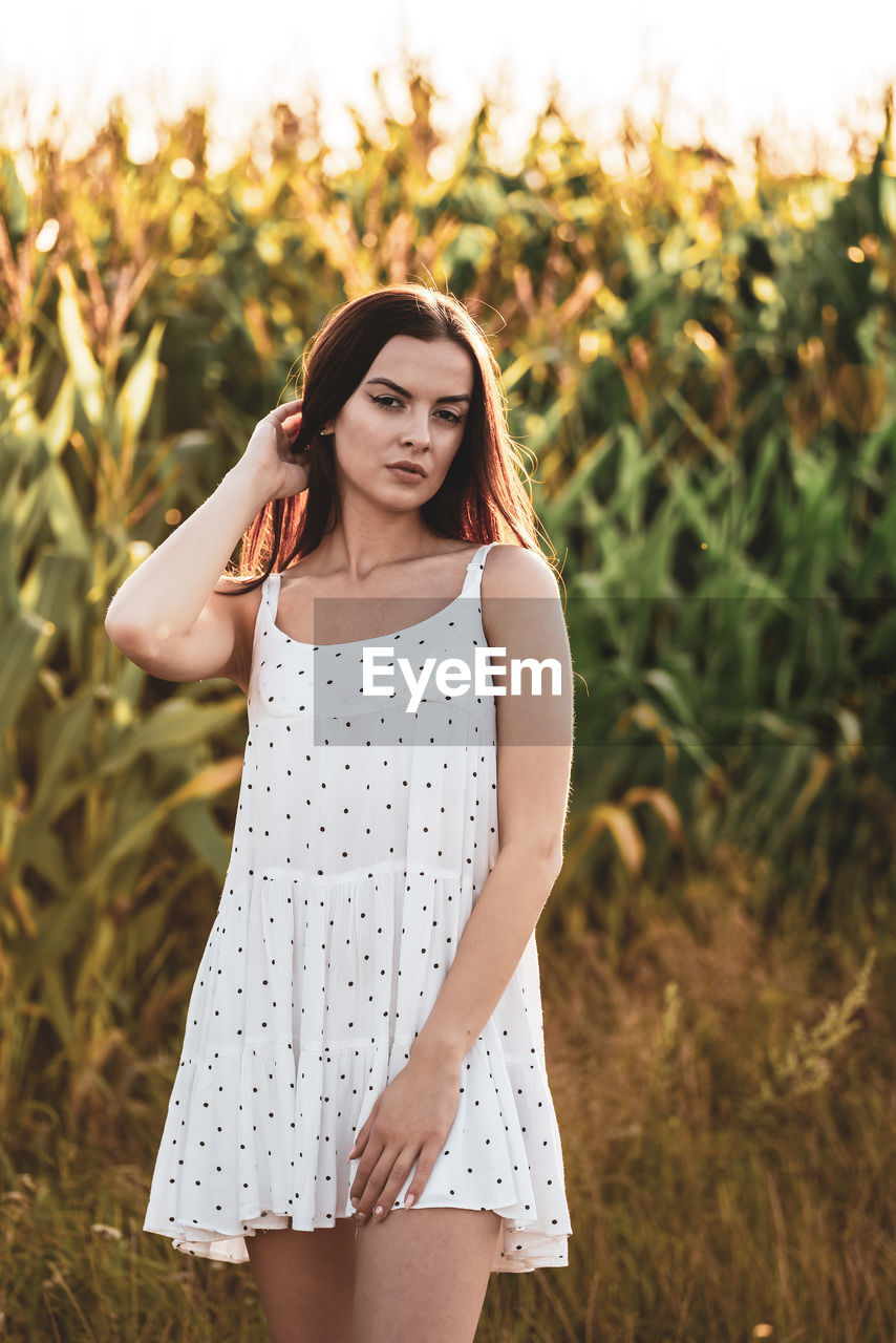 women, one person, young adult, adult, fashion, long hair, hairstyle, plant, nature, summer, clothing, standing, portrait, land, dress, rural scene, field, brown hair, landscape, three quarter length, sunset, smiling, sky, beauty in nature, happiness, outdoors, grass, leisure activity, lifestyles, sunlight, front view, looking, emotion, looking at camera, female, relaxation, environment, meadow, casual clothing, tranquility, agriculture, contemplation, plain, child, crop, day, photo shoot, teenager, spring, focus on foreground, sundress, carefree, cereal plant, yellow, tree, arts culture and entertainment, springtime