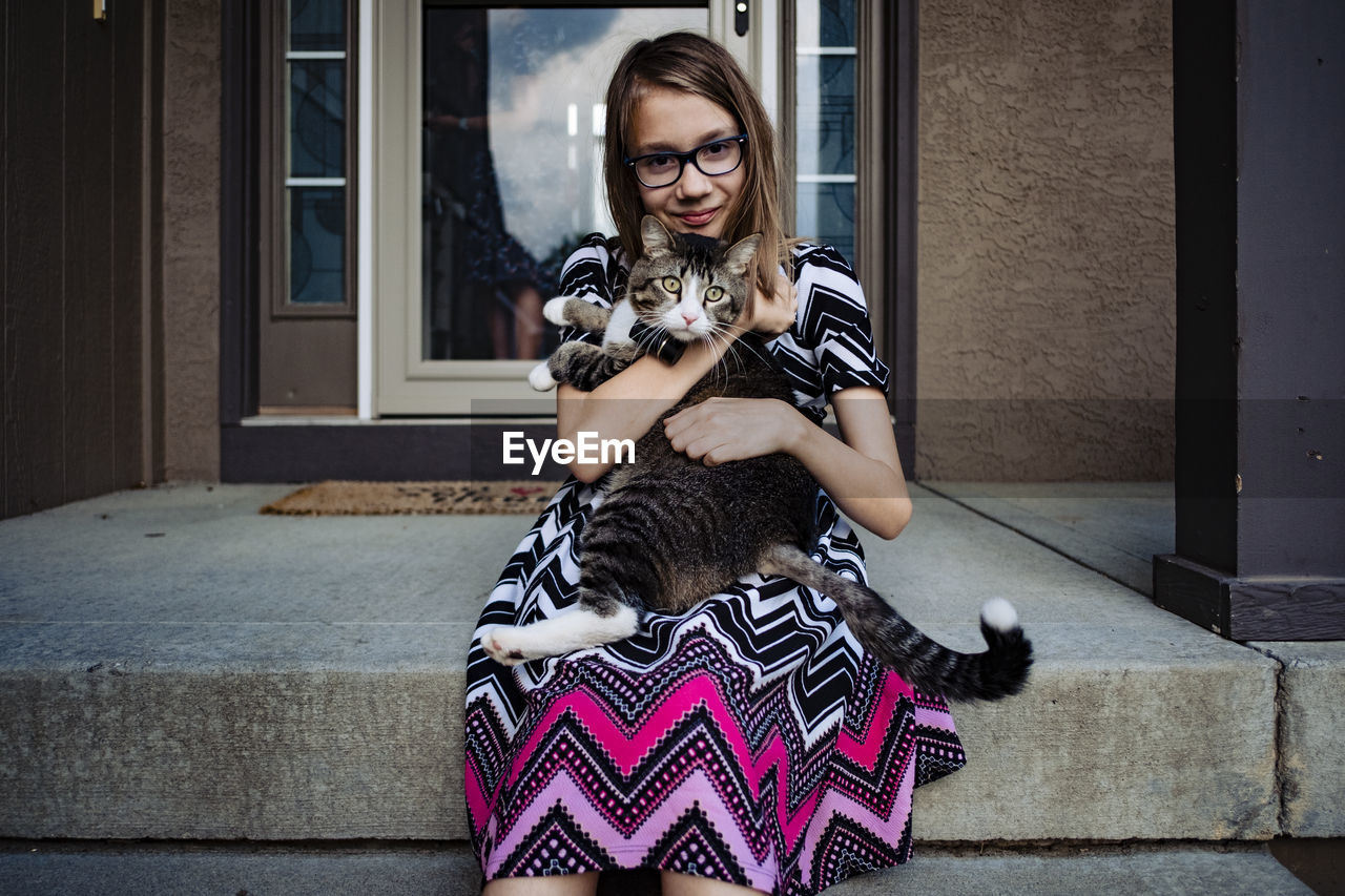 A pre teen girl holding her gray cat on the front porch
