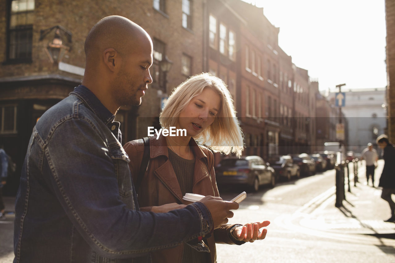 Couple using mobile phone while walking on city street