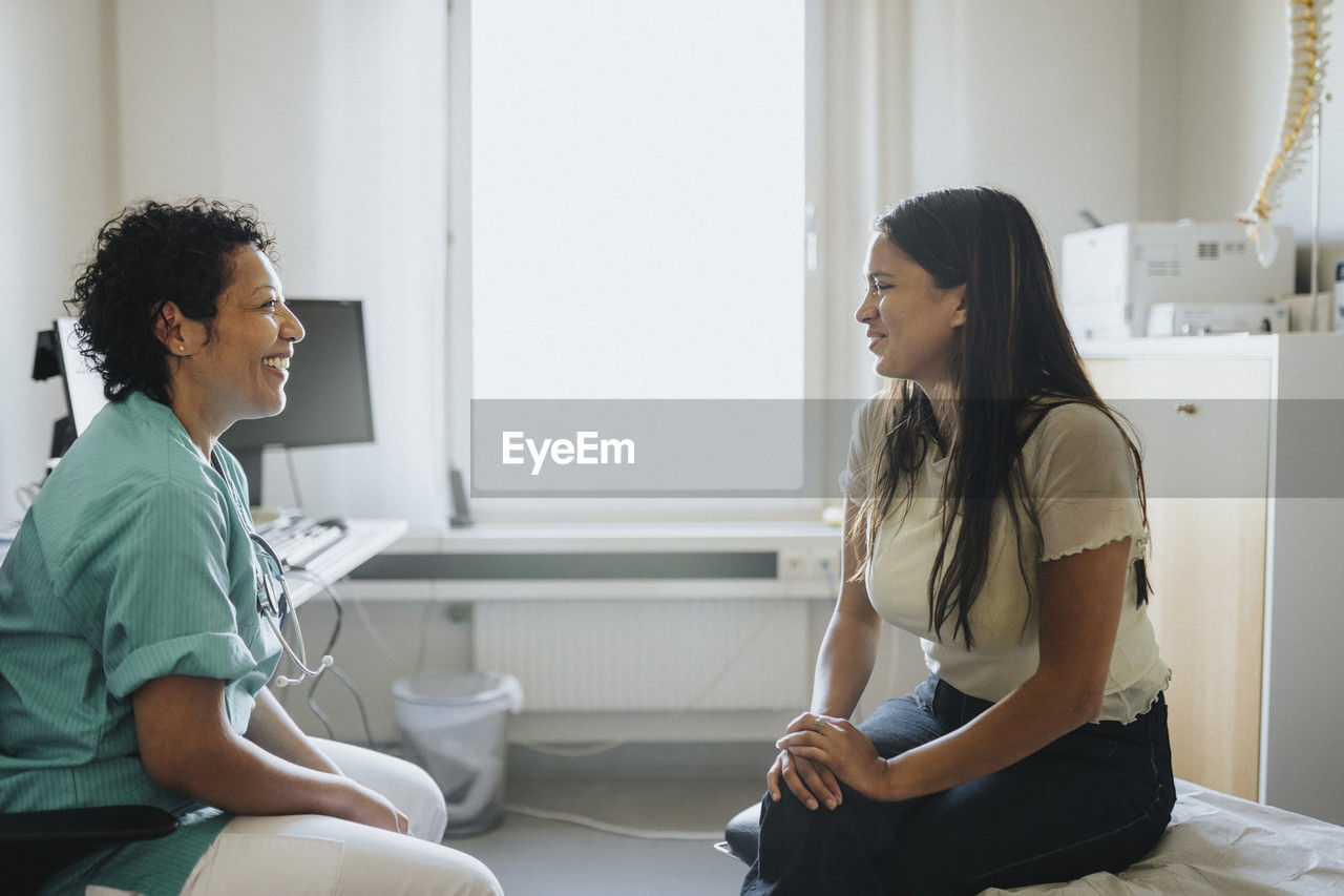 Smiling mature doctor and female patient discussing while sitting in clinic