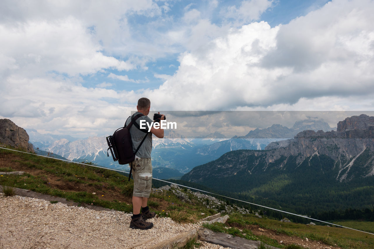 Side view of man standing on mountain against cloudy sky