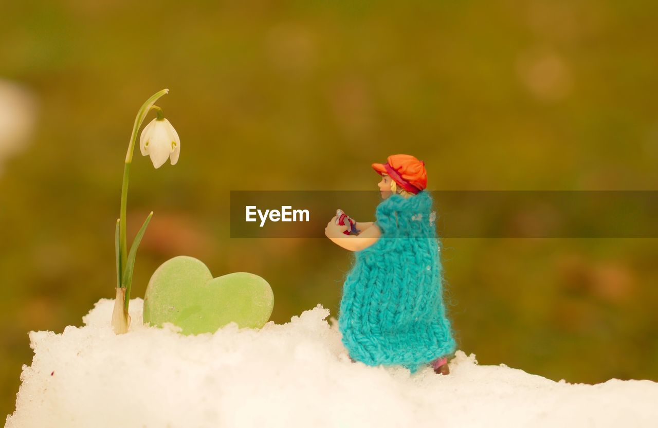 Close-up of figurine by snowdrop flower on snow