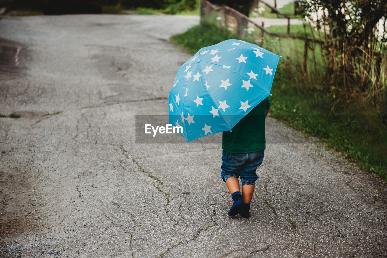 Back view of a child with an umbrella walking barefoot in the street