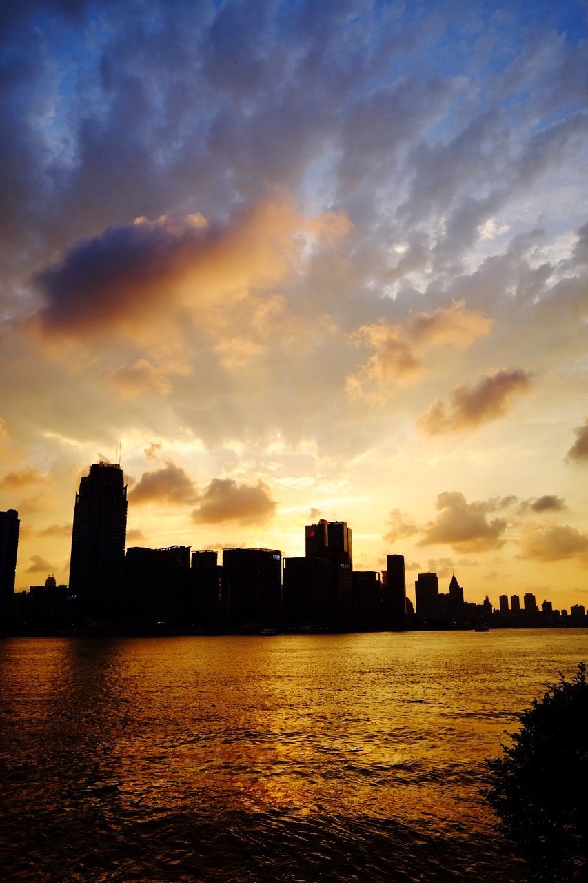 Silhouette buildings by sea against sky during sunset