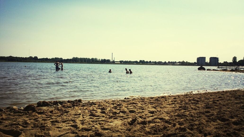 People swimming in calm ocean against clear sky