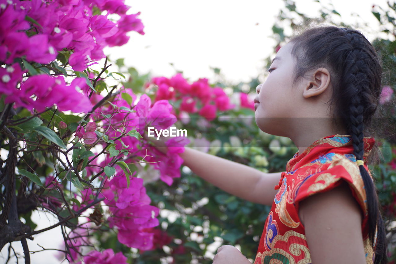 Low angle view of girl by pink flowering plants against sky