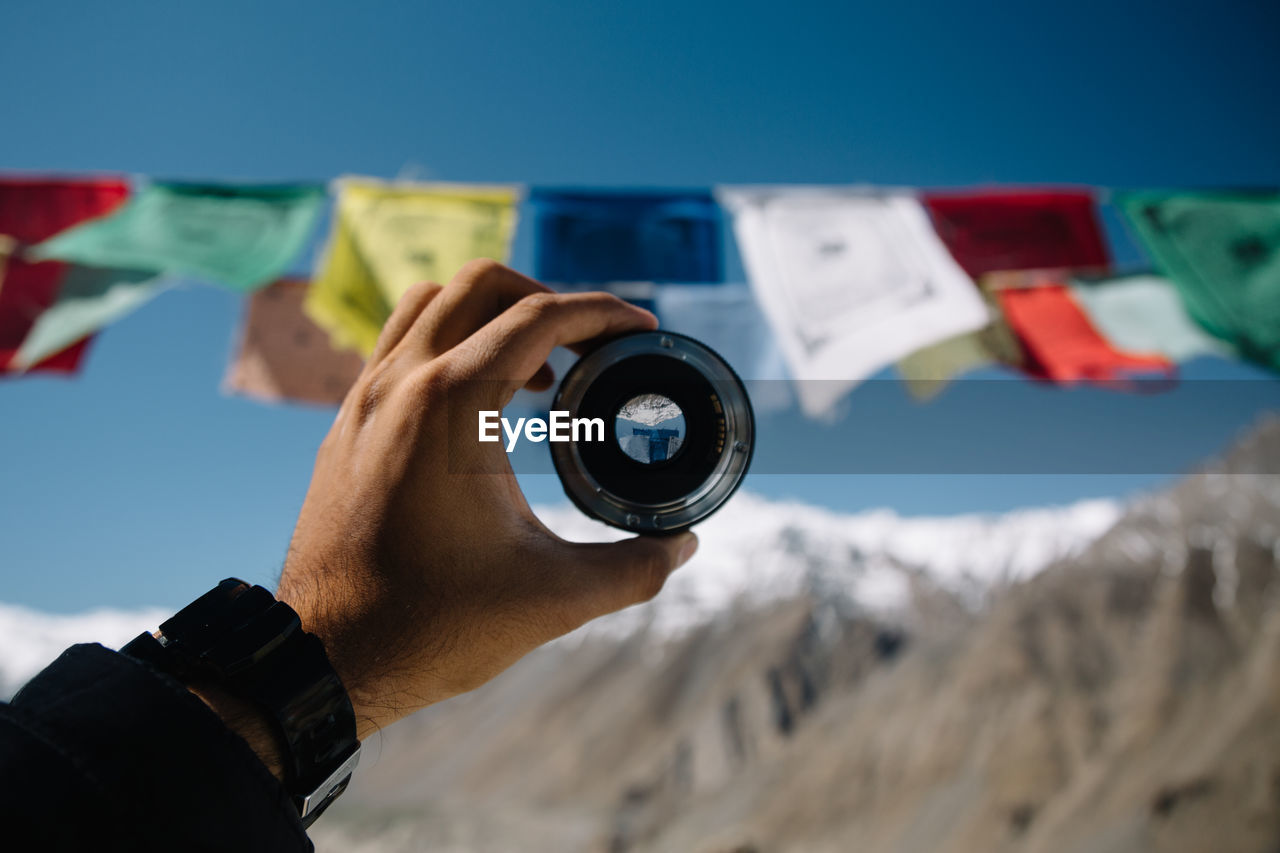 Close-up of hand holding camera lens against sky