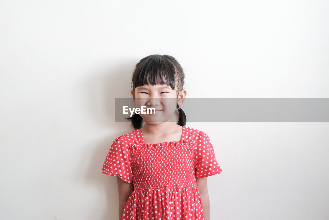 PORTRAIT OF SMILING GIRL STANDING AGAINST WALL