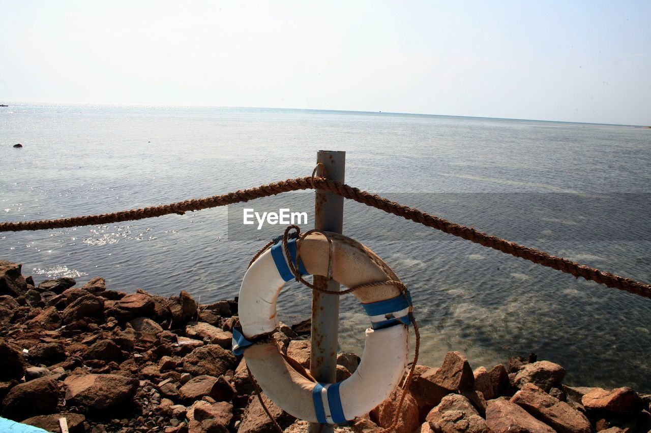 Inflatable ring on rope fence pole over groyne in sea against sky