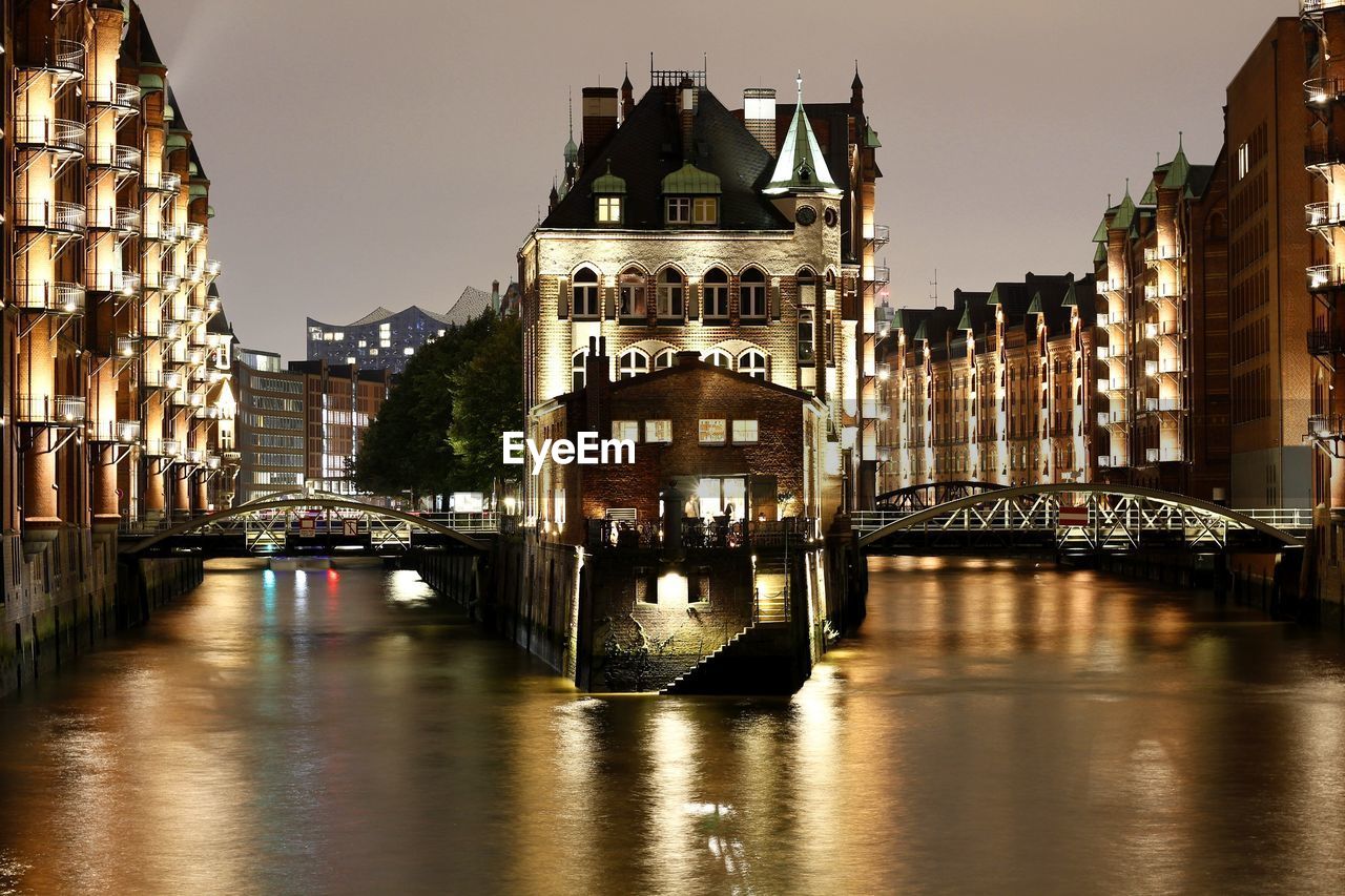 Illuminated buildings by river in city at night