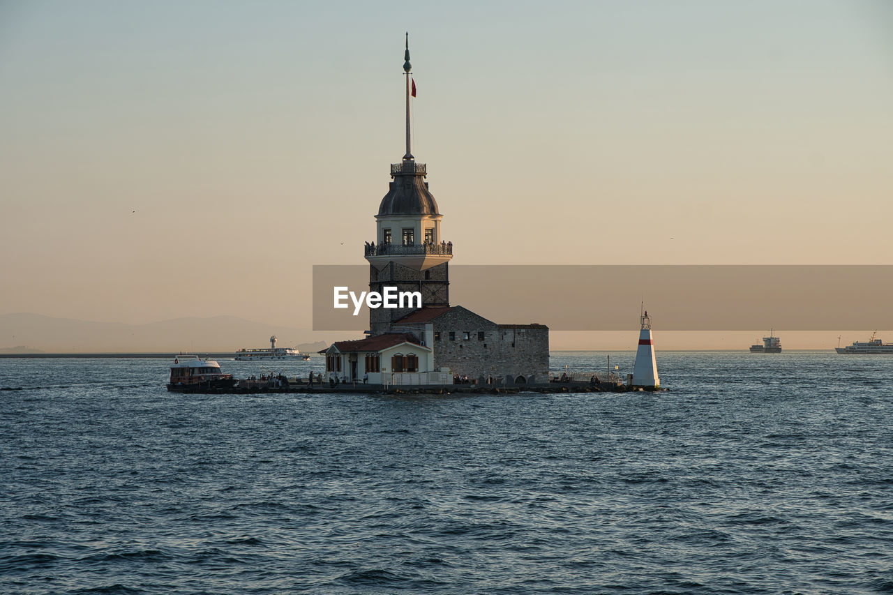 Lighthouse by sea against clear sky during sunset