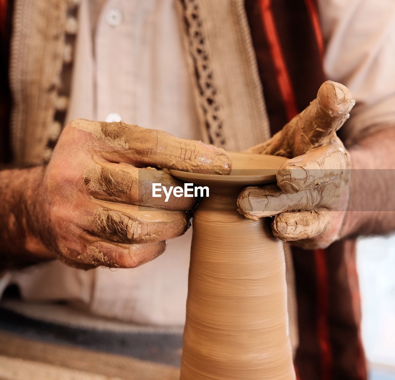 Midsection of potter molding clay on pottery wheel