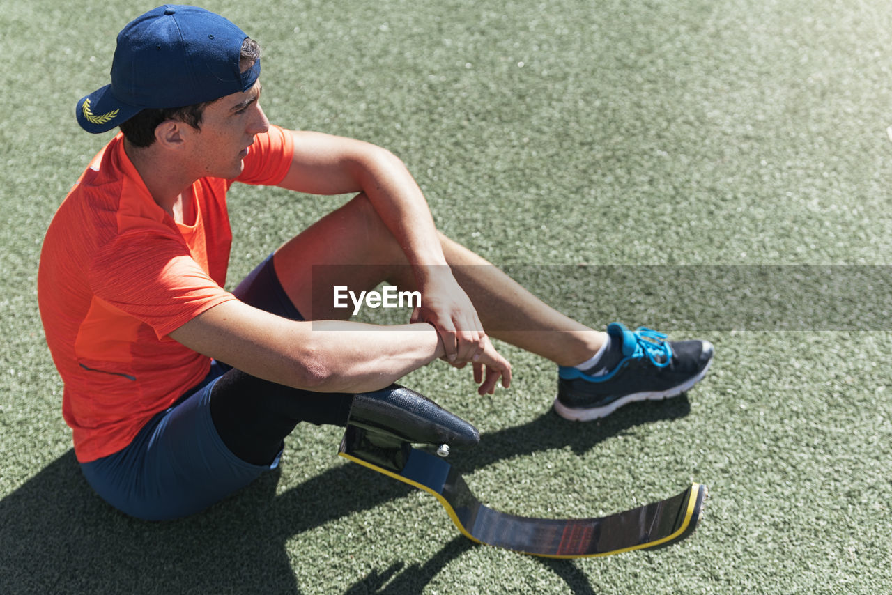 Full length of athlete with prosthetic leg sitting on field against sky