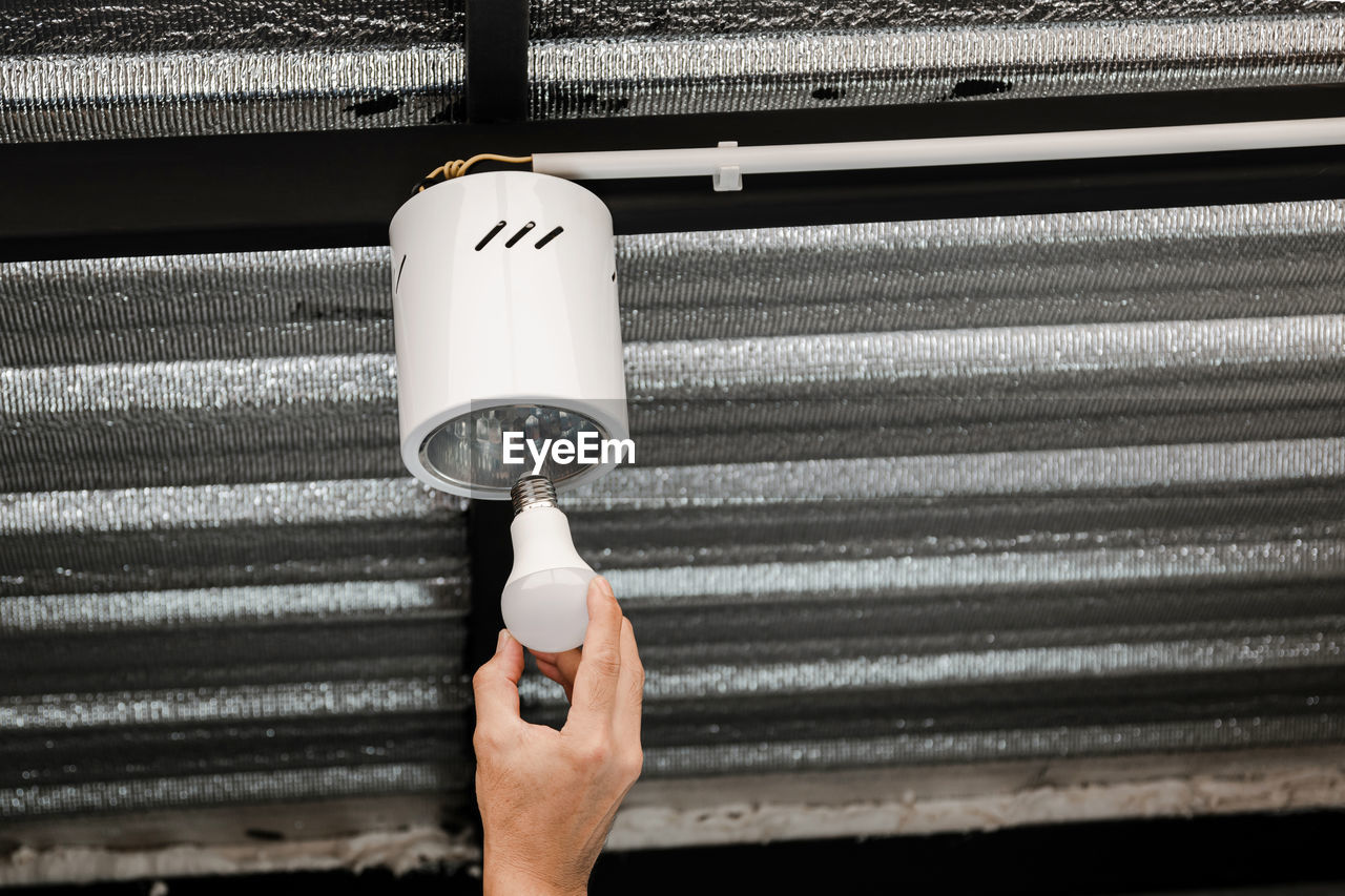 Close up human hand is installing an led light bulb in a circular ceiling lamp.